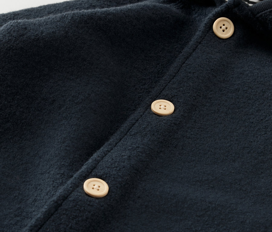 Detail modrého detského overalu s vlnou merino a svetlými gombíkmi.
