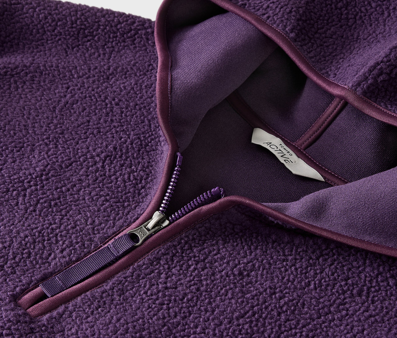 Detail fialovej fleecovej mikiny so zipsom a štítkom.