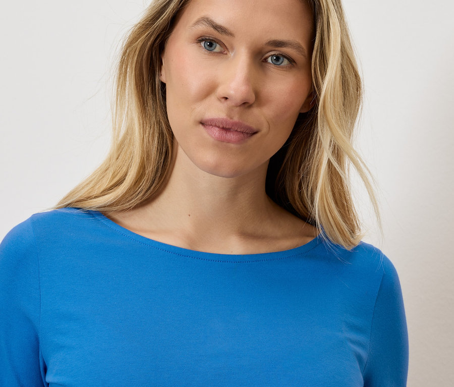 Portrét blondínky v modrom tope s dlhým rukávom.