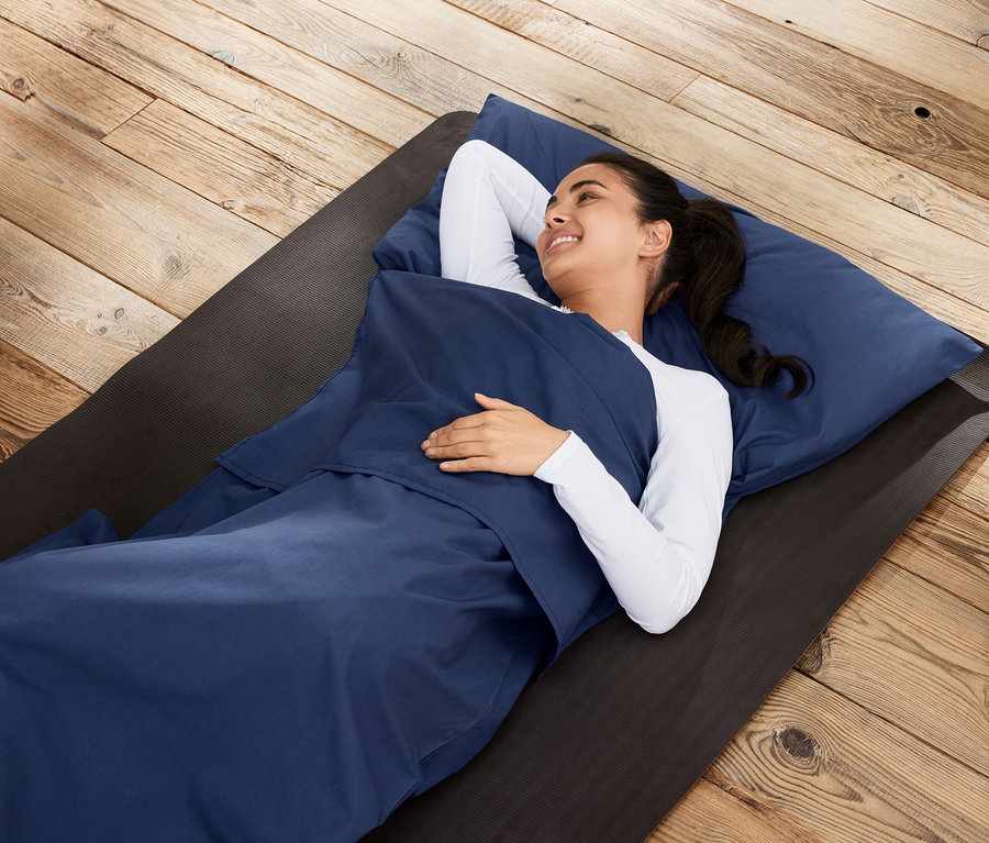 Žena leží vo vložke do spacieho vaku na podložke na drevenej podlahe.