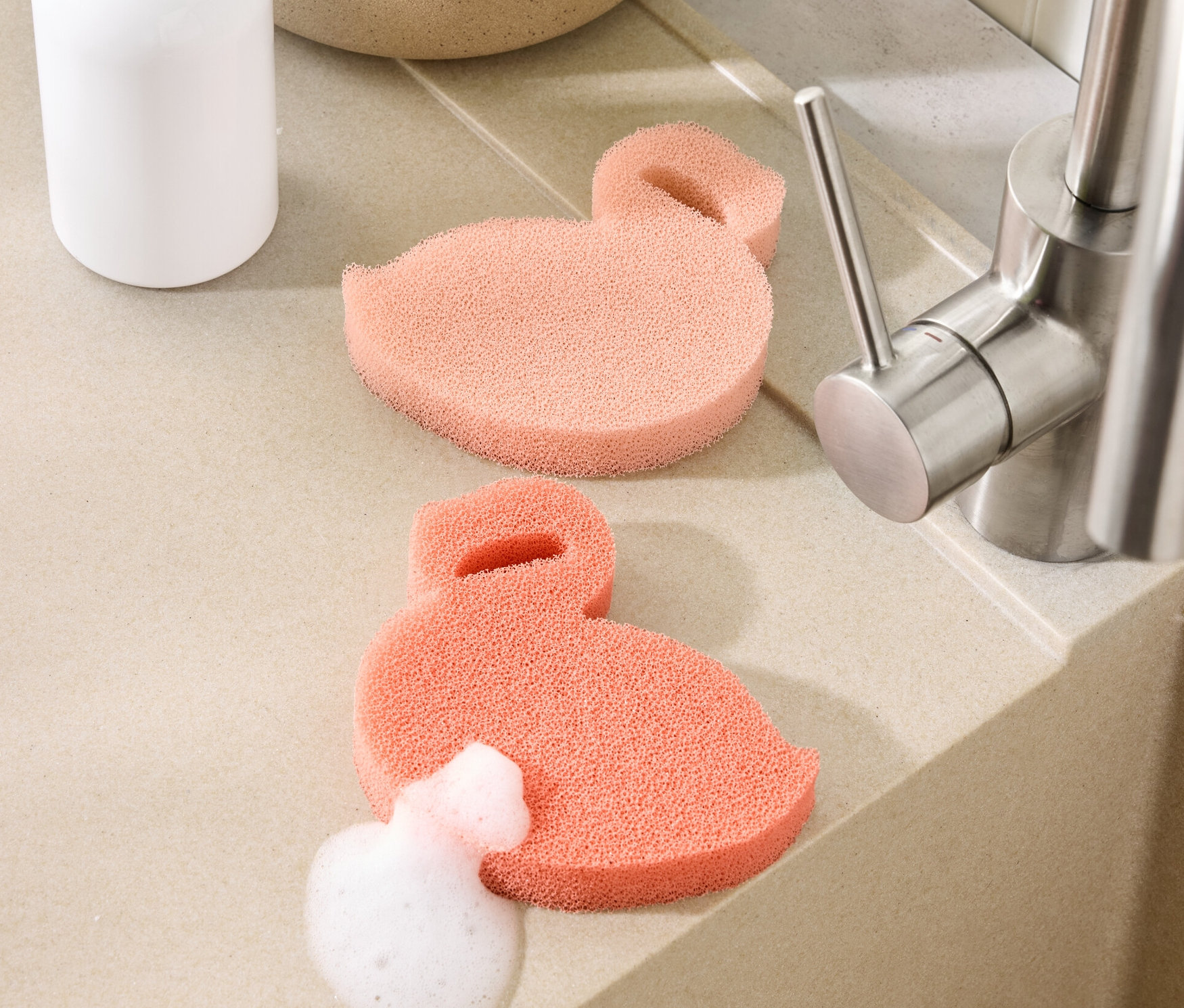 Dve silikónové hubky v tvare plameniaka ležia na linke pri dreze. Jedna z nich je pokrytá penou.