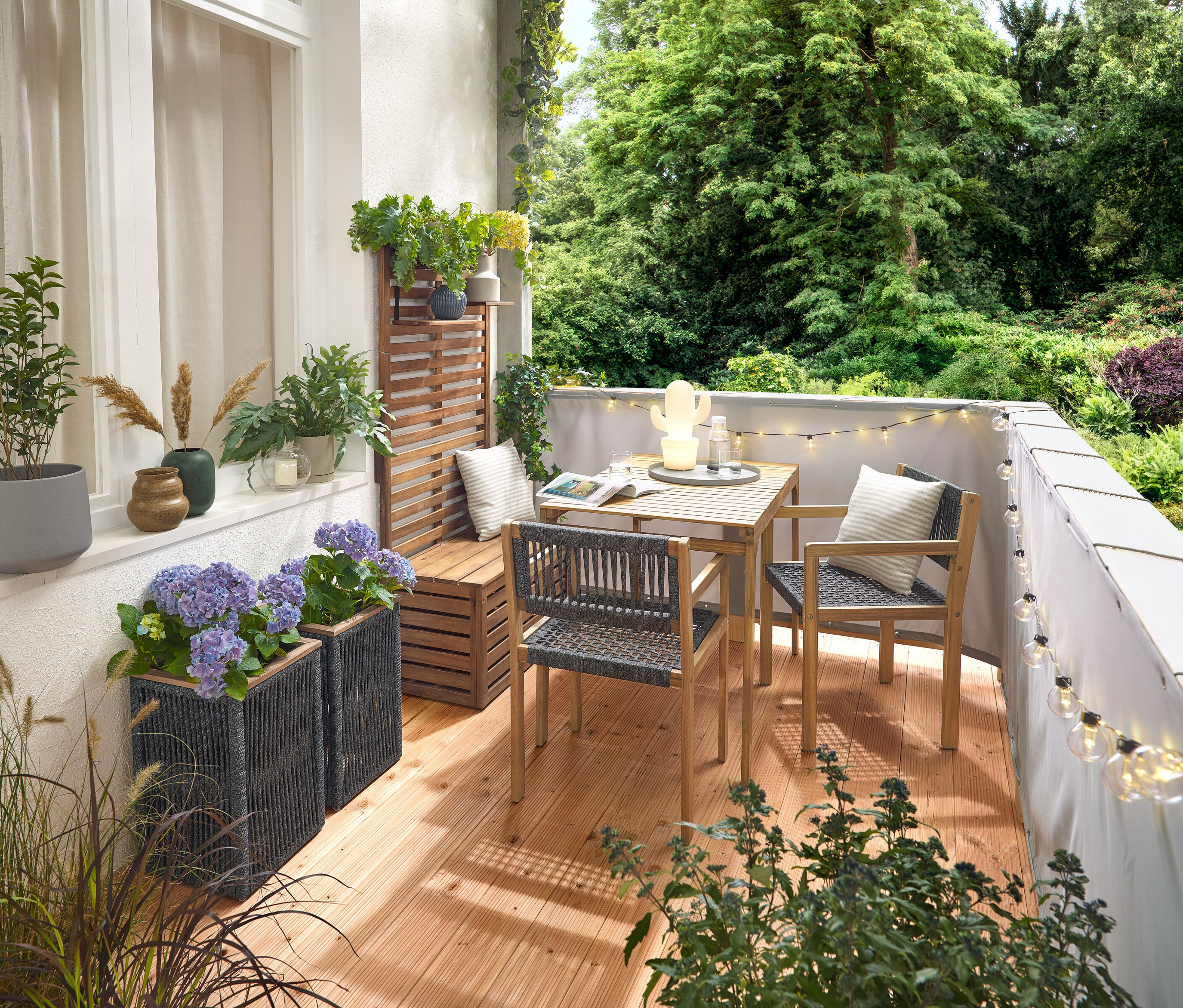 Zariadenie balkóna s balkónovou súpravou s textilnou výplňou, sivou balkónovou clonou a ochranou proti vetru, vonkajšou LED reťazou s adaptérom, kvetináčom s textilnou výplňou, vonkajšou LED akumulátorovou stolnou lampou, kaktusom a 2 vonkajšími vankúšmi s ľanovým povrchom.