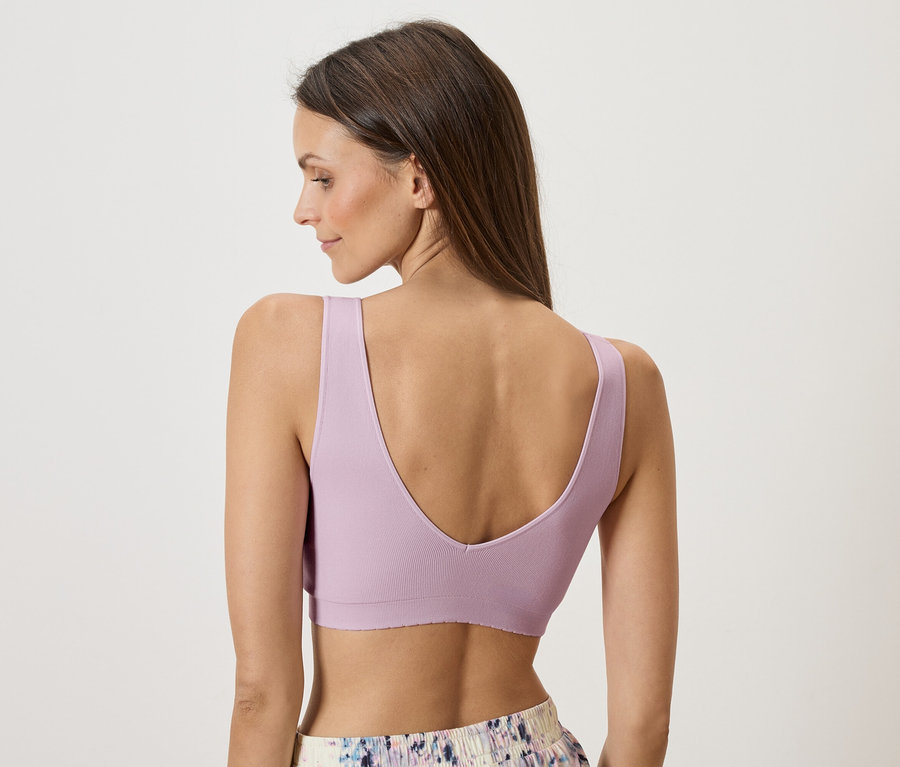 Pohľad zozadu na ženu s hnedými vlasmi, oblečenú v fialovom športovom tope a vzorovaných šortkách.