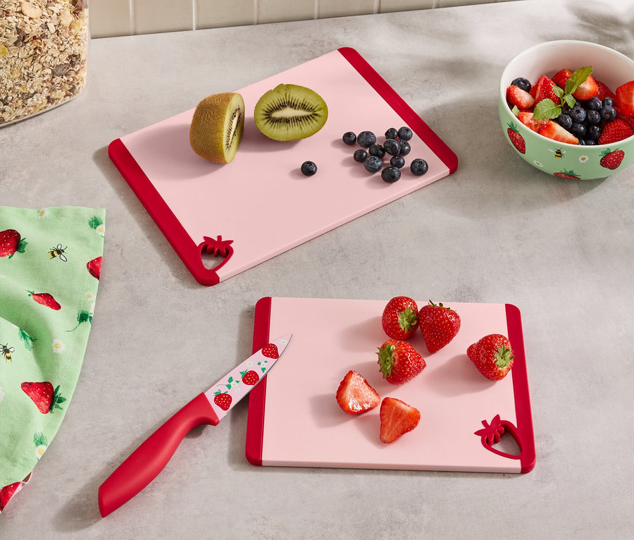 Na kuchynskej linke sú dve ružové dosky na krájanie s červeným okrajom, nádoba s cereáliami, miska s bobuľami, utierka a nôž.