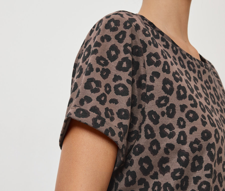 Detailný záber osoby v hnedom tričku s čiernym leopardím vzorom.