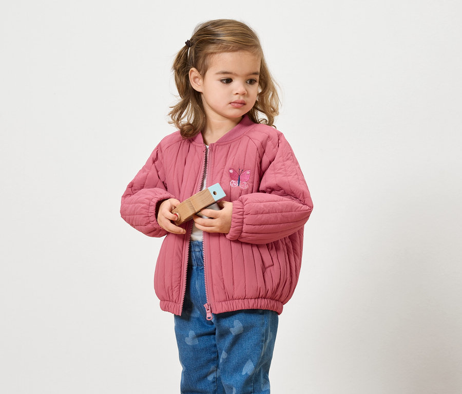 Dievča v ružovej bunde drží drevenú hračku.