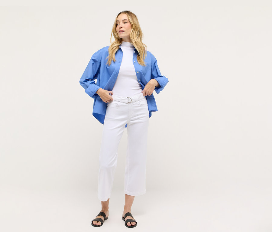 Žena má na sebe biele skrátené džínsy Angels Denim »Linn City« a modrú košeľu.