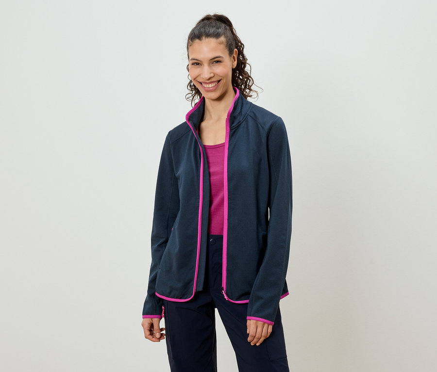 Žena s konským chvostom má na sebe tmavomodrú flísovú bundu s ružovými akcentmi, ružový top a tmavomodré nohavice.