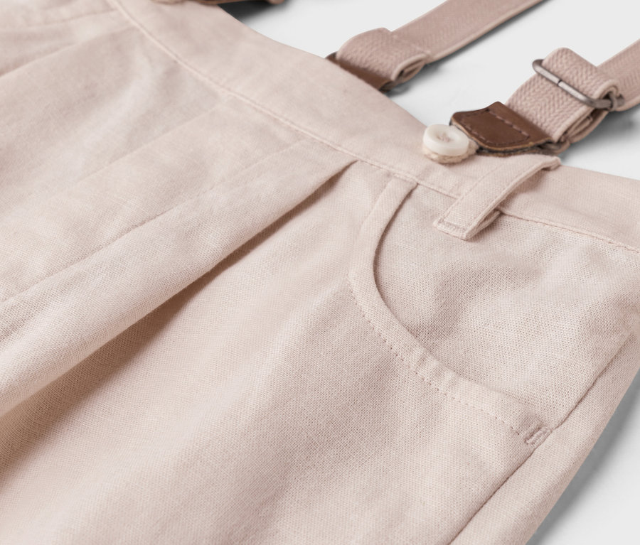 Detailný záber svetlobéžových nohavíc s trakmi, gombíkom a vreckom.
