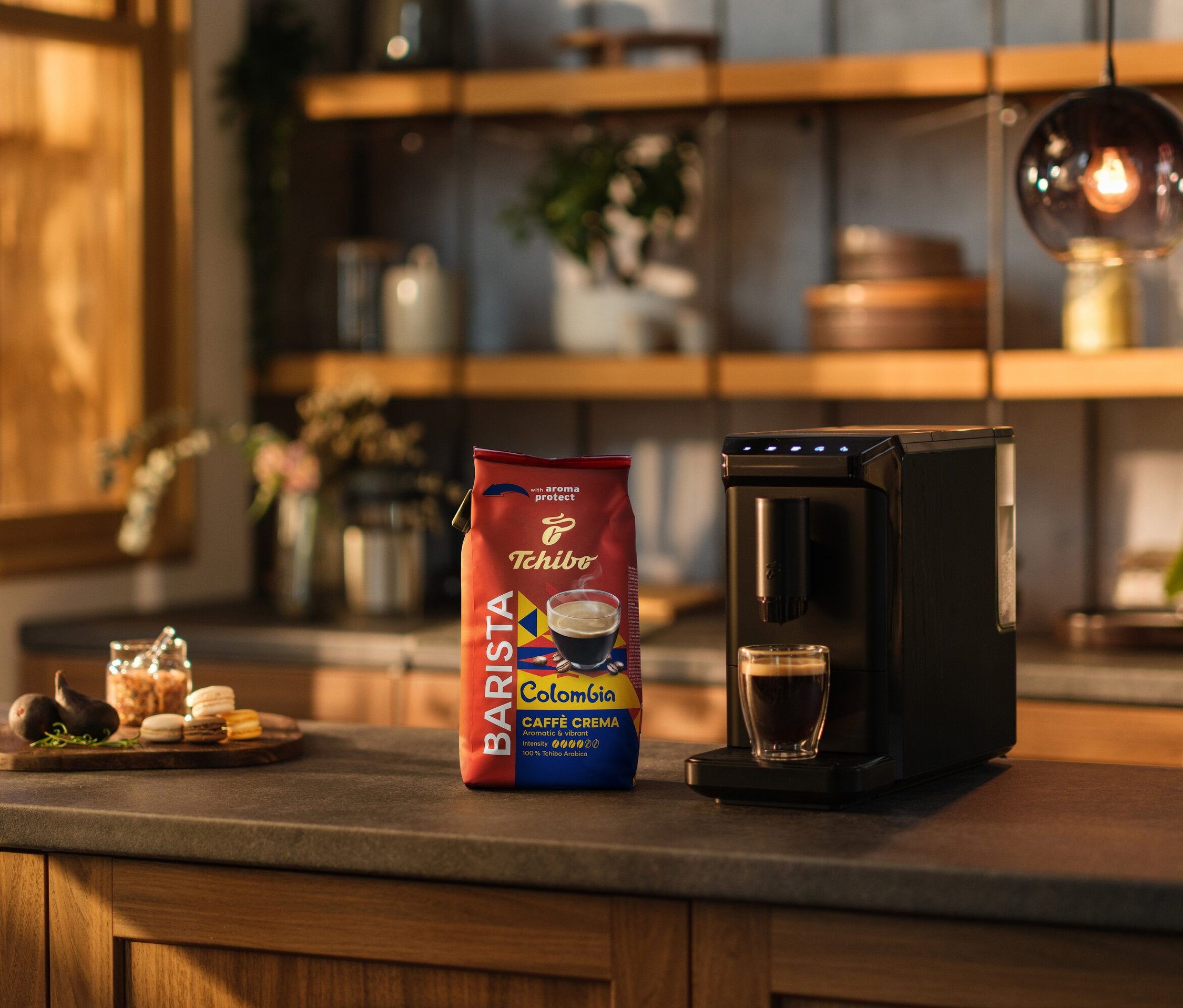 Na kuchynskej linke stojí kávovar, šálka kávy a balenie BARISTA Origins Colombia - 1 kg, zrnková káva.