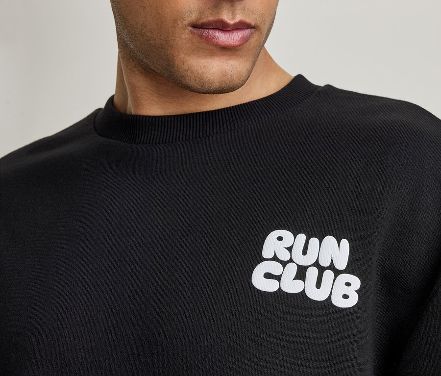 Detail muža v čiernej mikine s bielym nápisom 'RUN CLUB'.