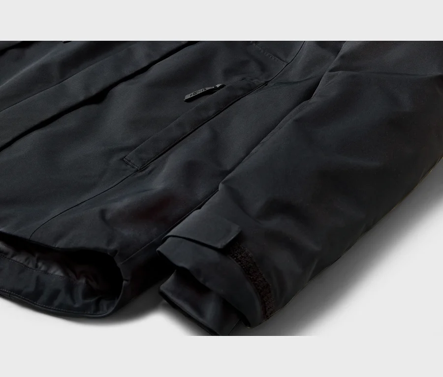 Detail čiernej bundy s vreckom na zips na hrudi s logom na jazdci a nastaviteľnou manžetou rukáva na suchý zips.