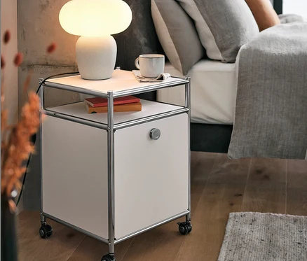 Stolová lampa so skleneným tienidlom stojí na kovovom kontajneri na kolieskach »CN3« s výklopnou doskou, biely, vedľa postele.