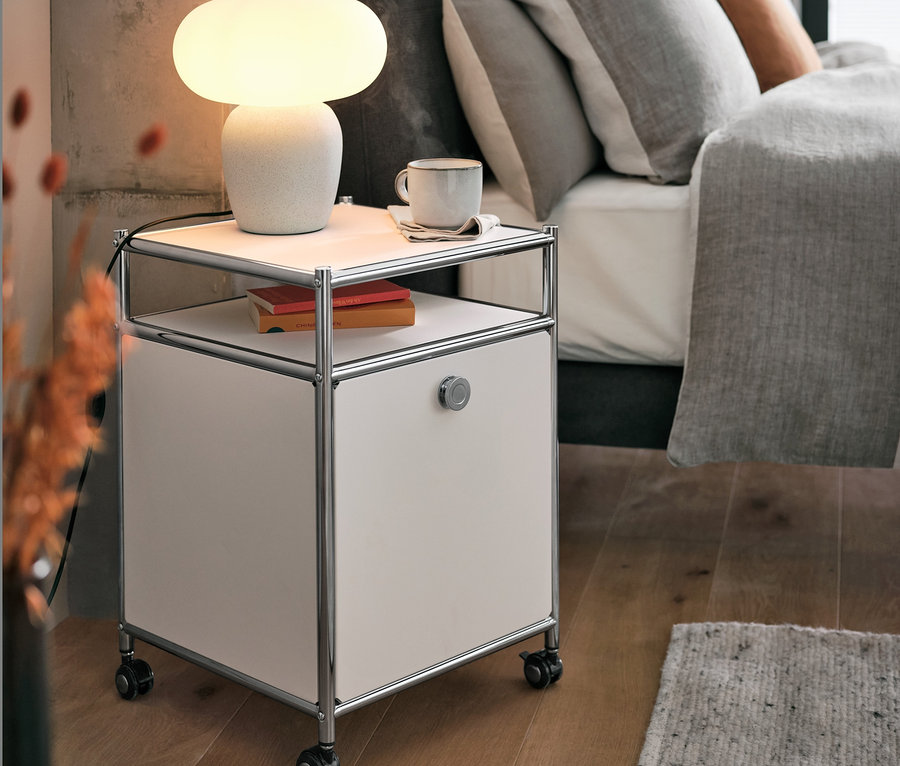 Stolová lampa so skleneným tienidlom stojí na kovovom kontajneri na kolieskach »CN3« s výklopnou doskou, biely, vedľa postele.