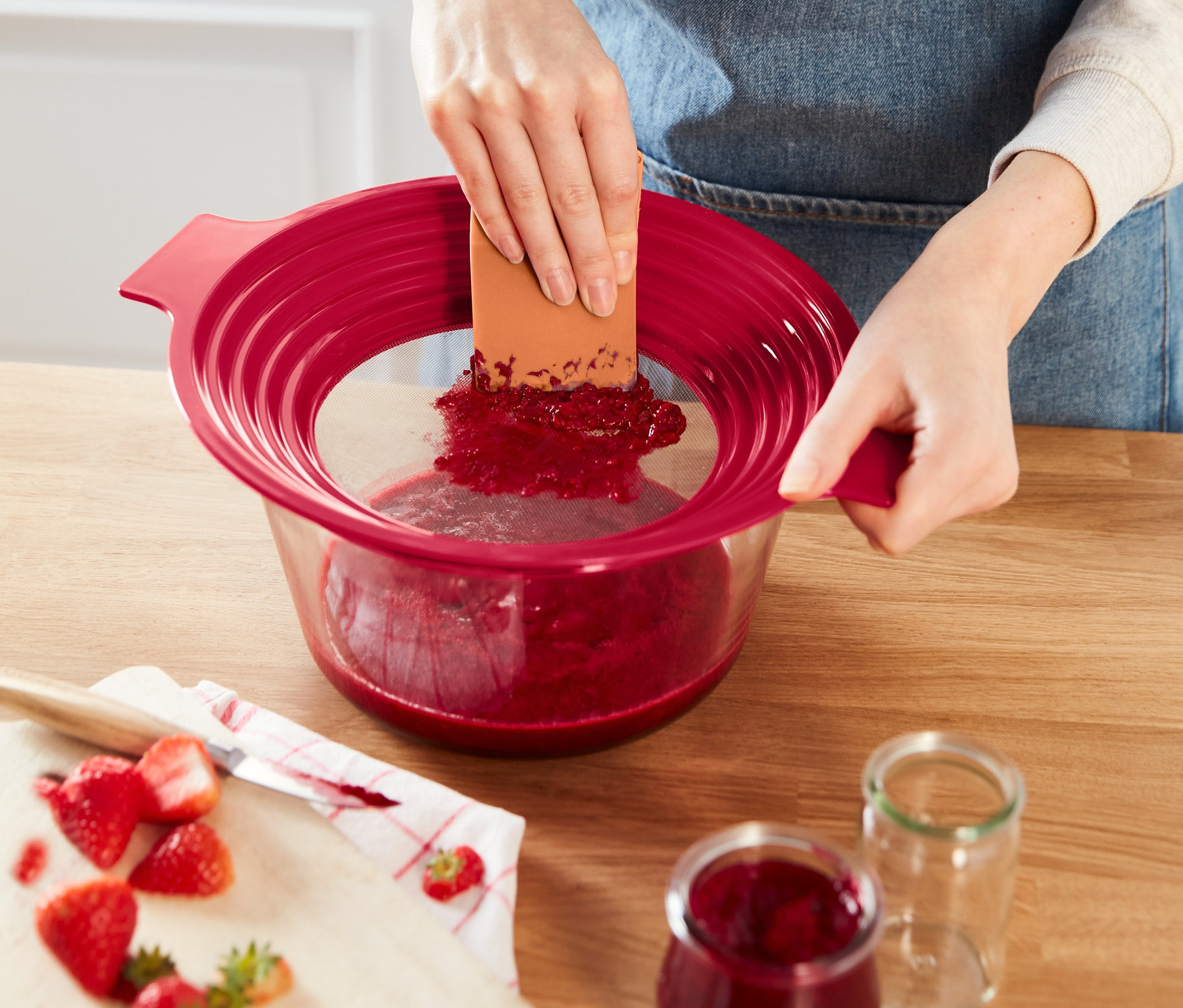 Žena pretláča jahody cez červené sito 2 v 1: sito na preosievanie múky a pasírovanie.