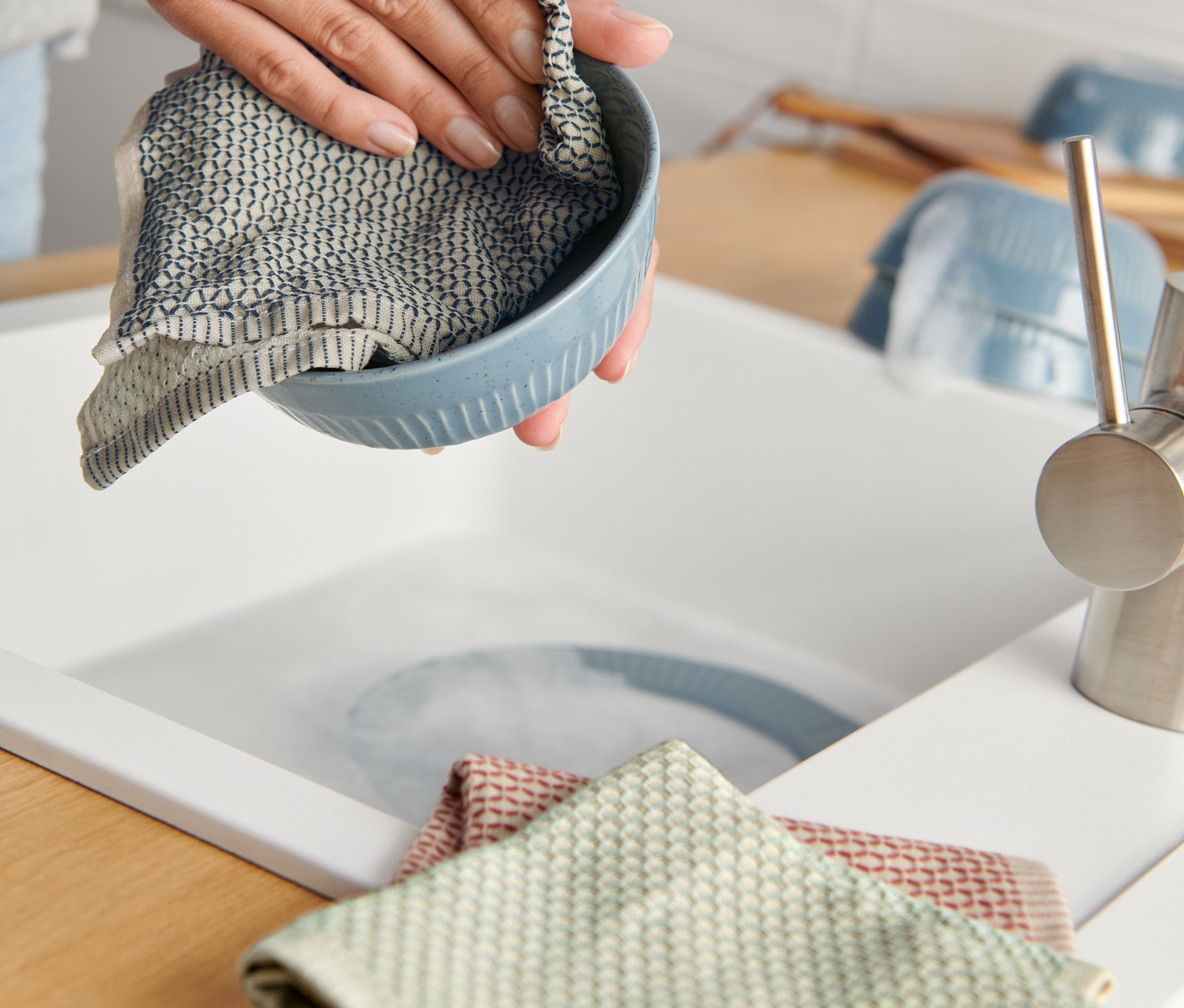 Žena utiera modrú misku handričkou na riad (3 ks) pri dreze.