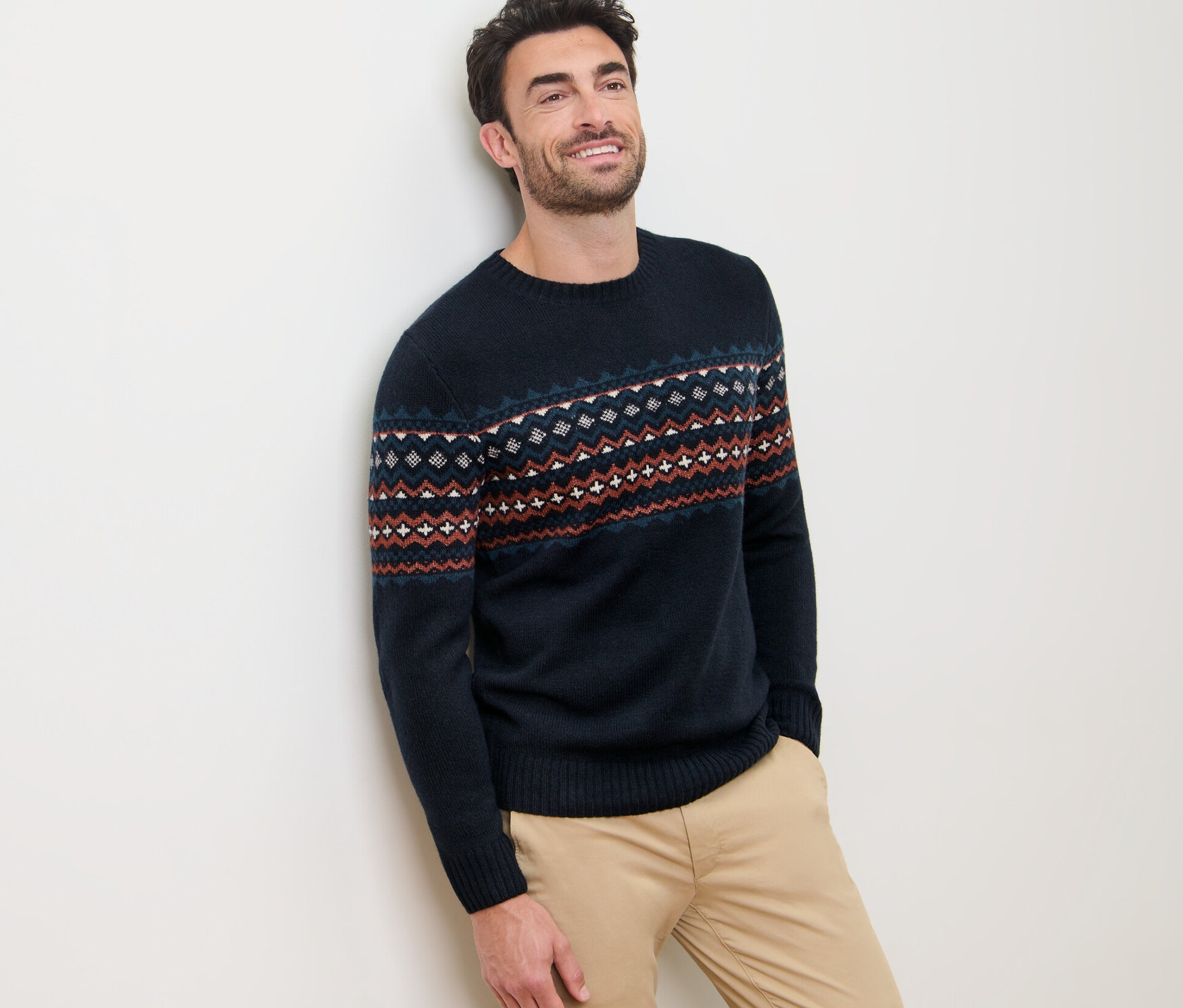 Muž opretý o stenu má na sebe pletený pulóver.