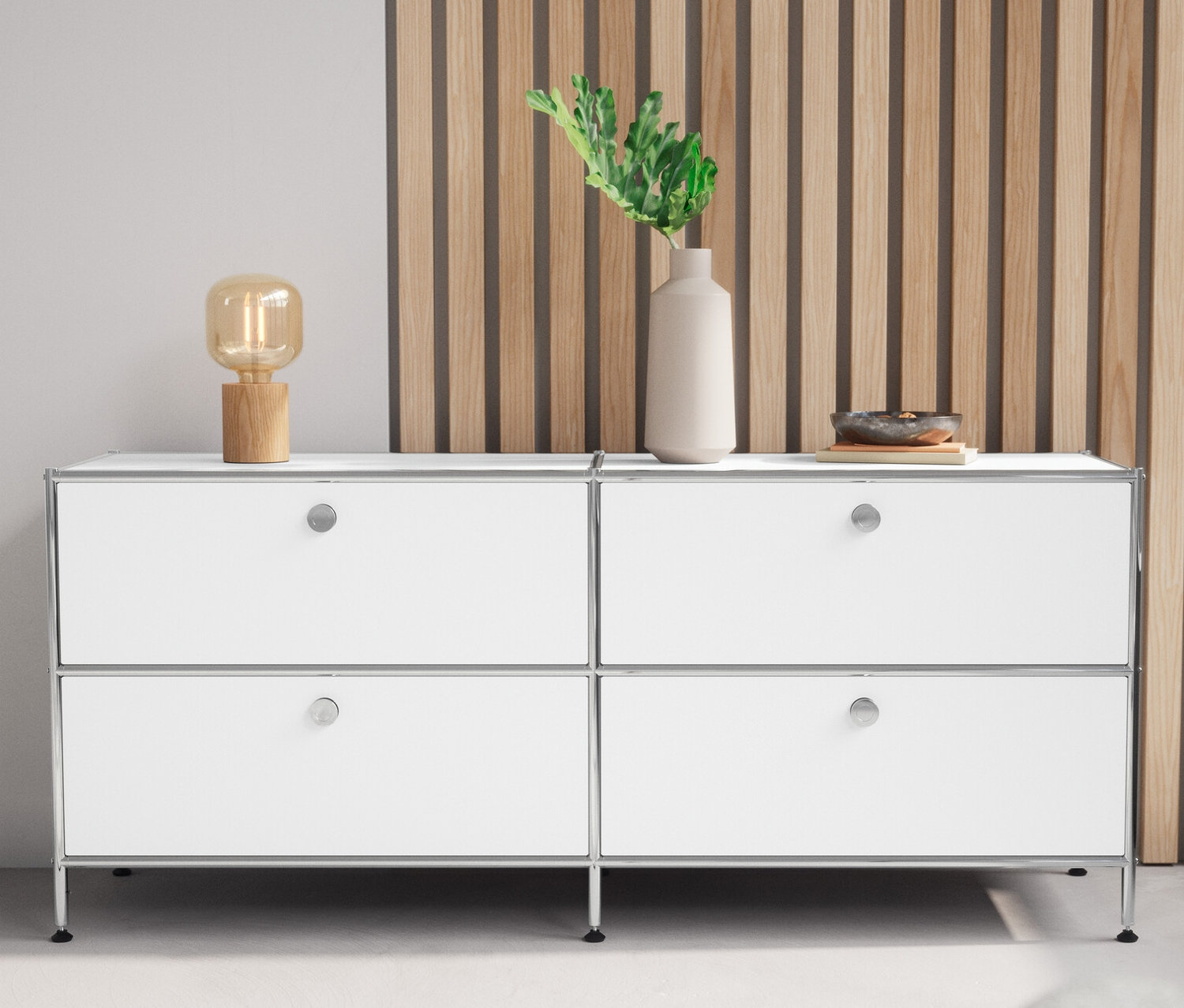 Biela kovová nízka skrinka »CN3« so 4 zásuvkami a stolová lampa z dreva stoja vedľa seba.