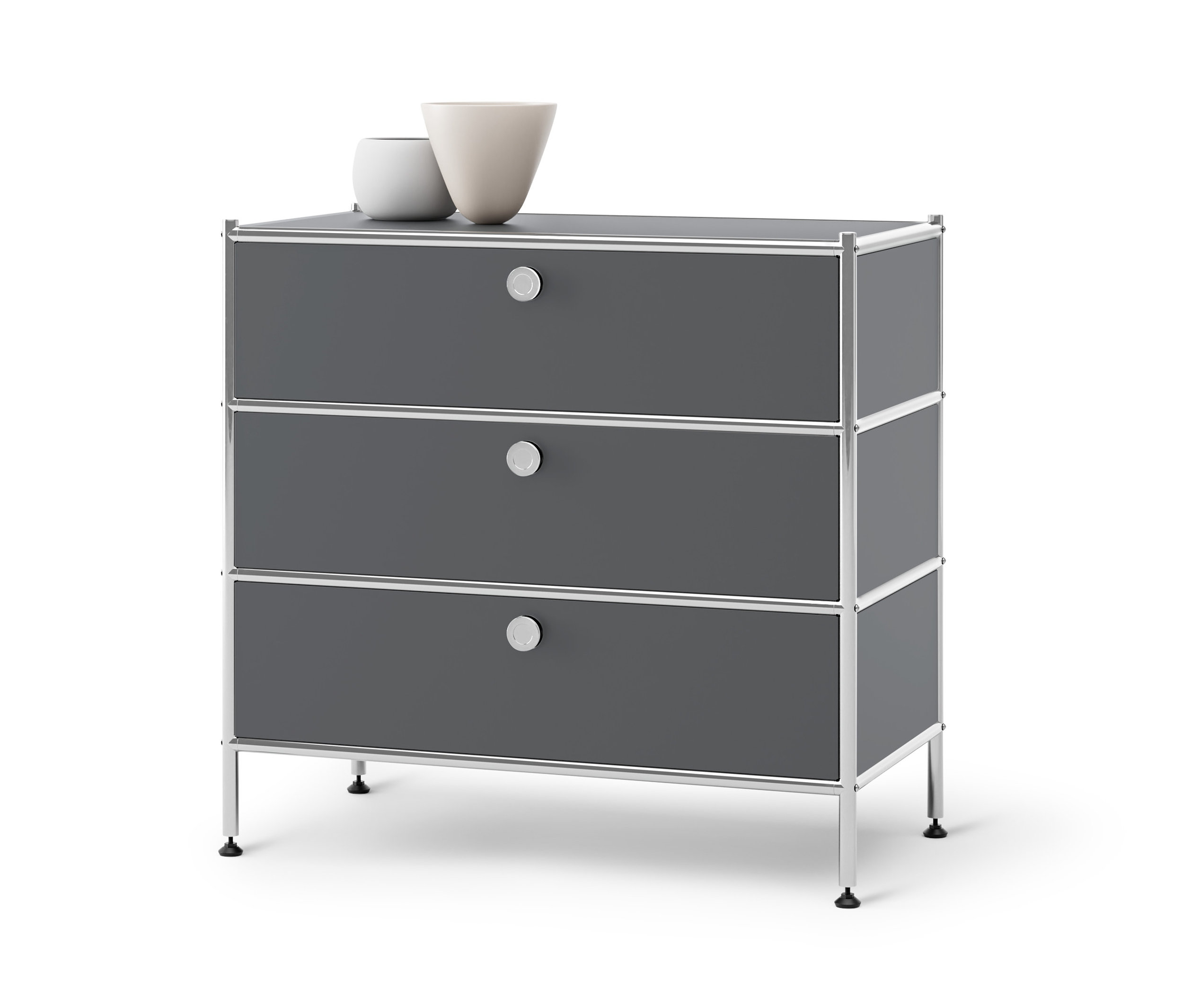 Sivá kovová komoda »CN3« s 3 zásuvkami. Hore stoja dve vázy.