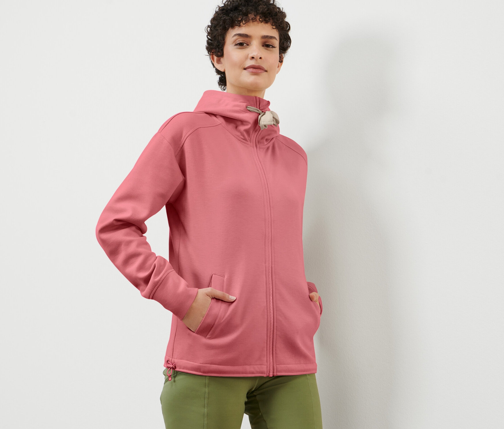 Žena pózuje v ružovej mikine s kapucňou.