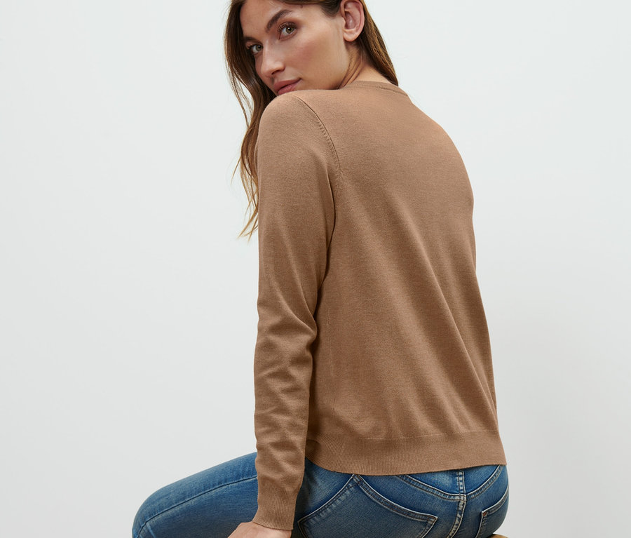 Žena sedí na drevenej stoličke a má na sebe kardigán z jemného úpletu.