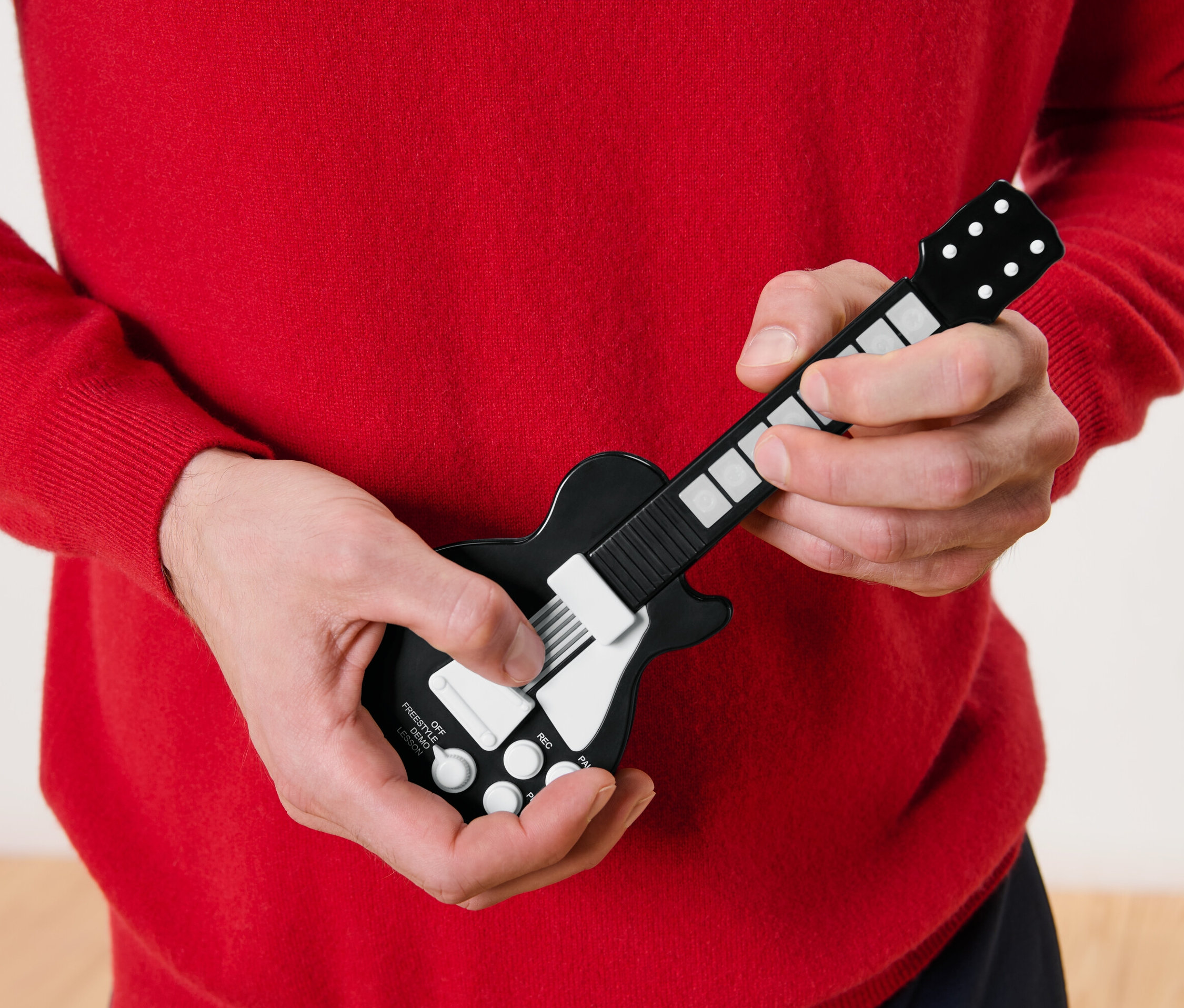 Muž v červenom svetri hrá na prstovú gitaru.