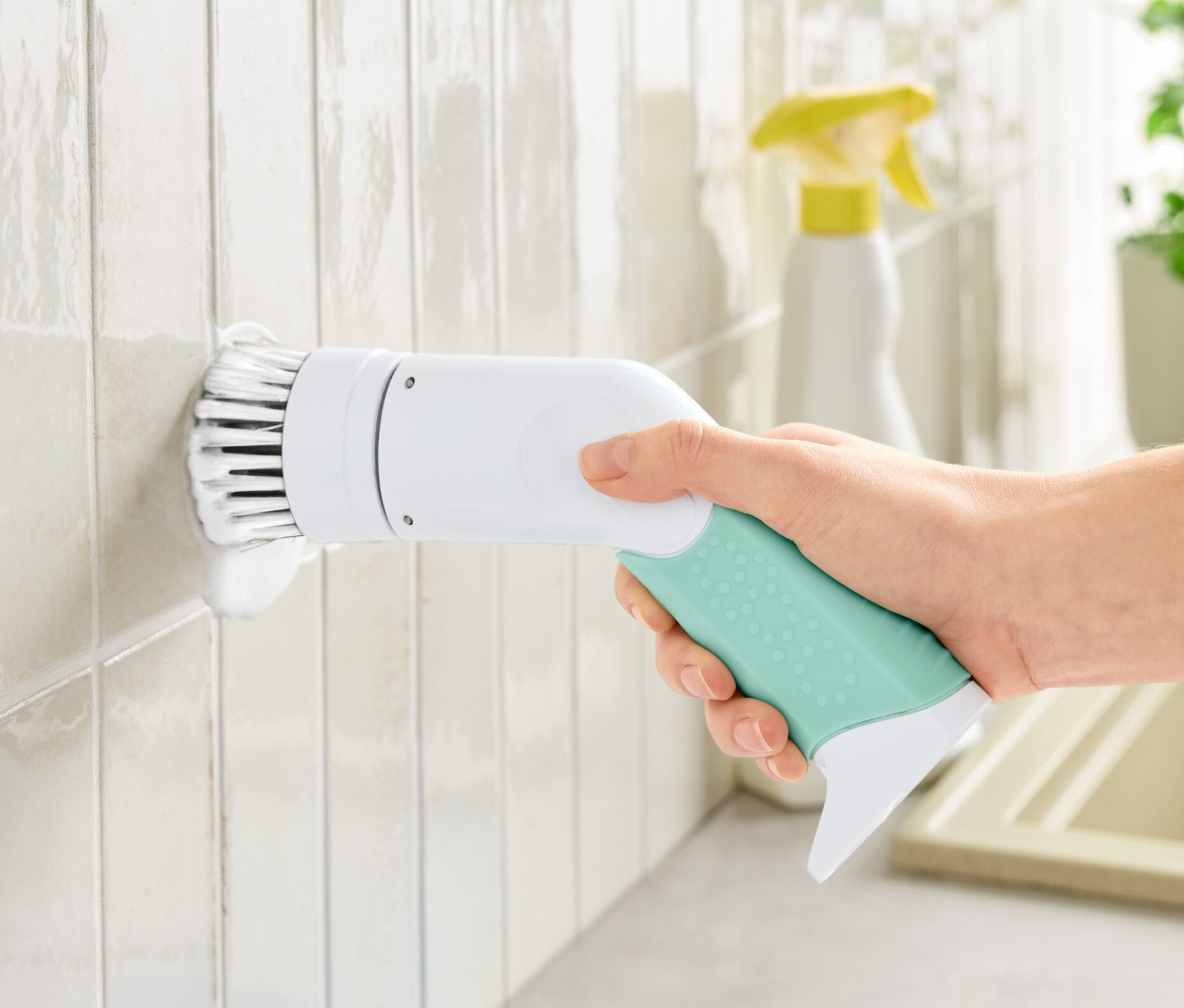 Ruka drží elektrickú čistiacu kefu, profesionálnu a čistí ňou biele dlaždice.