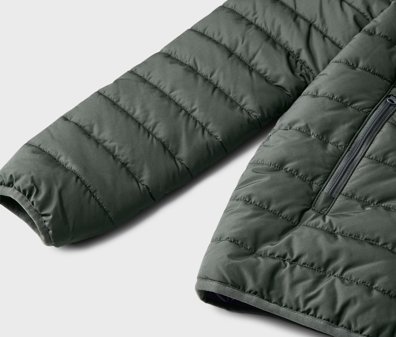 Detail detskej prešívanej bundy, tmavozelenej farby.