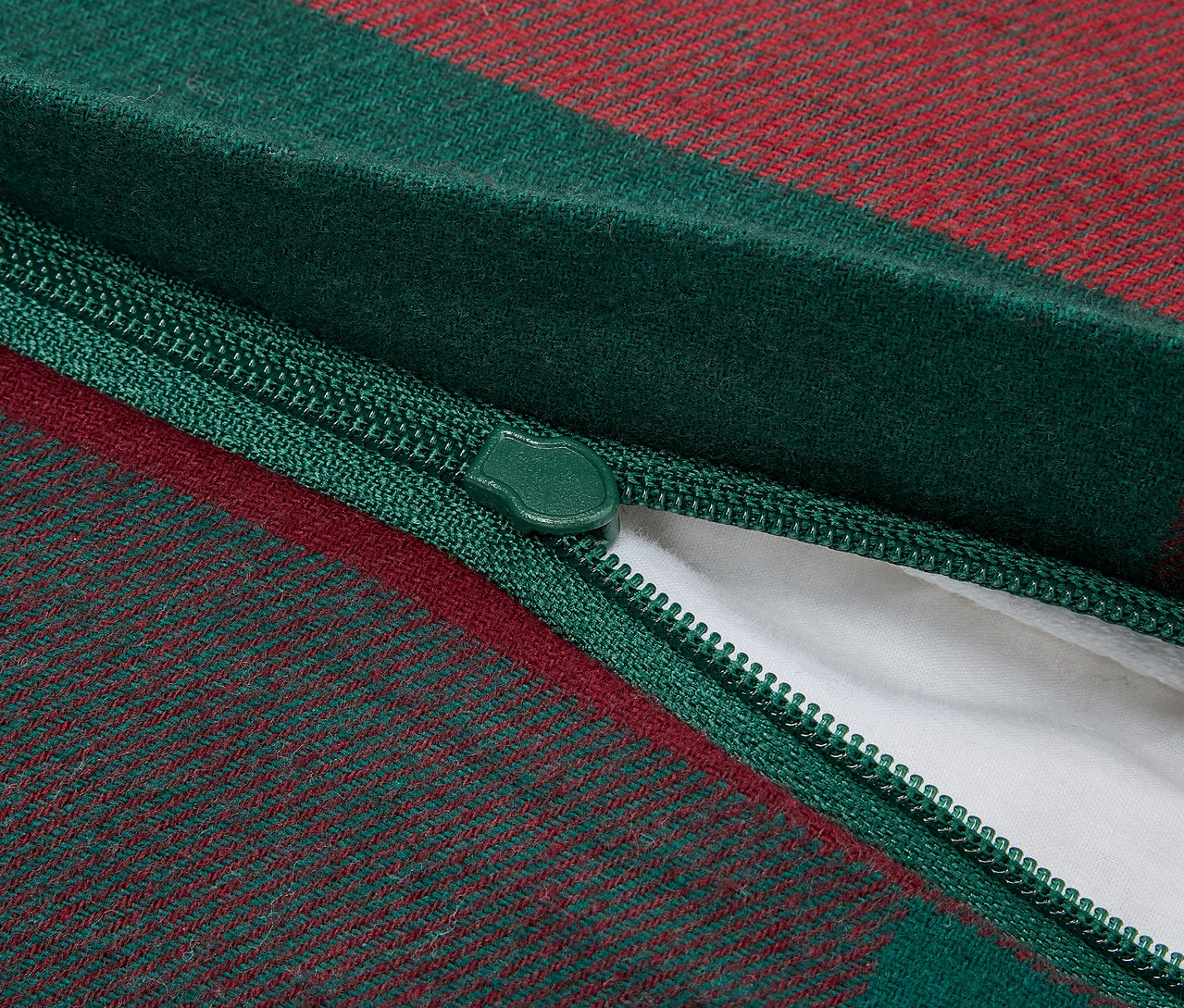 Detailný záber na zips zeleno-červenej kockovanej obliečky na vankúš, ktorý odhaľuje bielu vnútornú výplň.