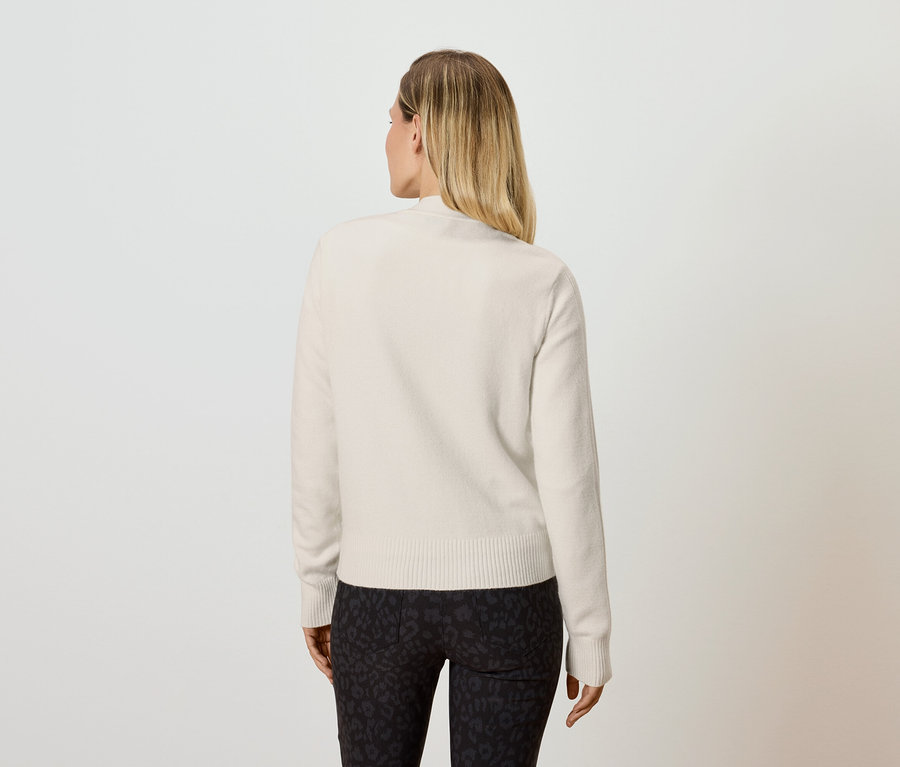 Pohľad zozadu na blondínu v krémovom svetri a čiernych legínach.