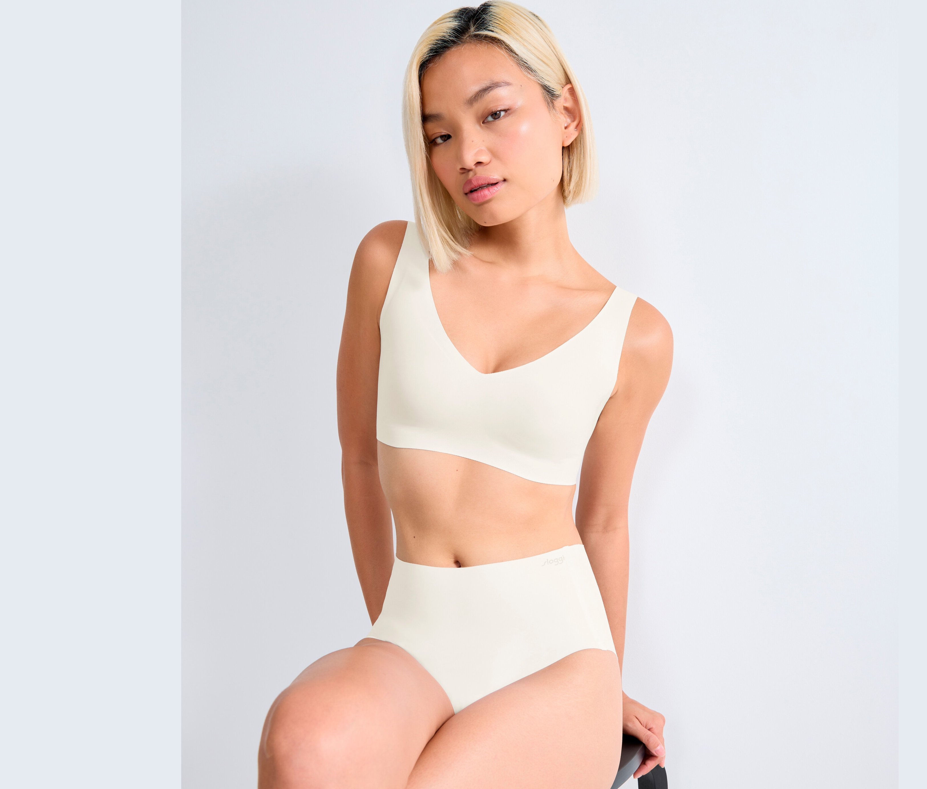 Žena sedí a má na sebe bielu braletku sloggi ZERO Feel 2.0 a nohavičky.