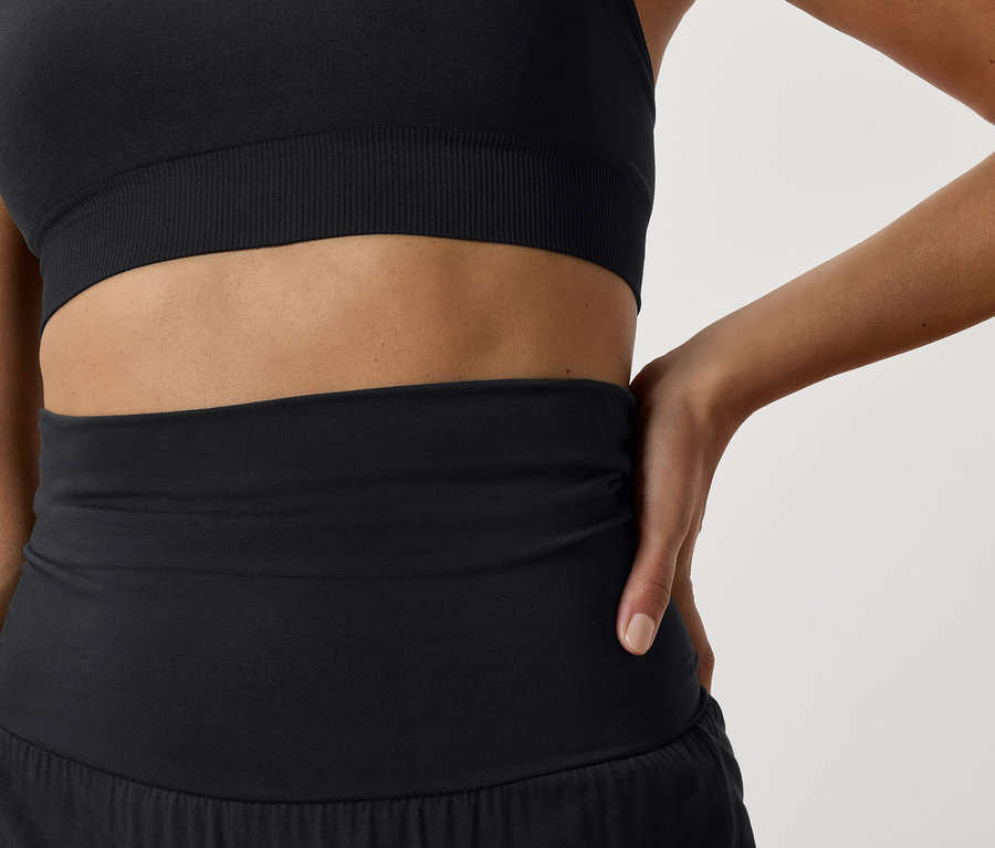 Detail ženy v čiernej športovej podprsenke a čiernych športových šortkách.