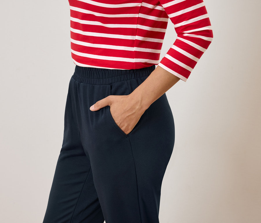 Žena s rukou vo vrecku tmavomodrých nohavíc a červeno-bielym pruhovaným tričkom.