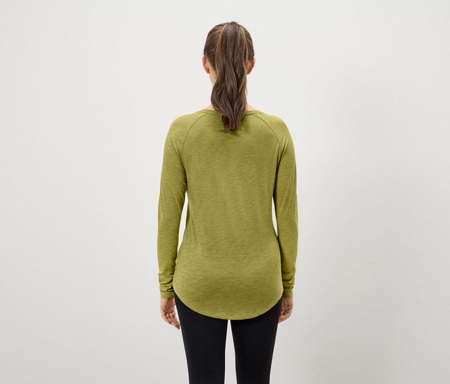 Pohľad zozadu na ženu s hnedými vlasmi zopnutými do copu, ktorá má na sebe olivovozelené tričko s dlhým rukávom a čierne legíny.