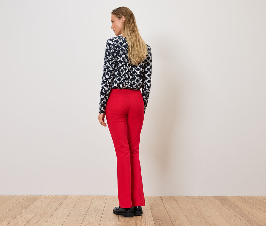 Žena stojí chrbtom, má na sebe vzorovanú blúzku a červené nohavice.