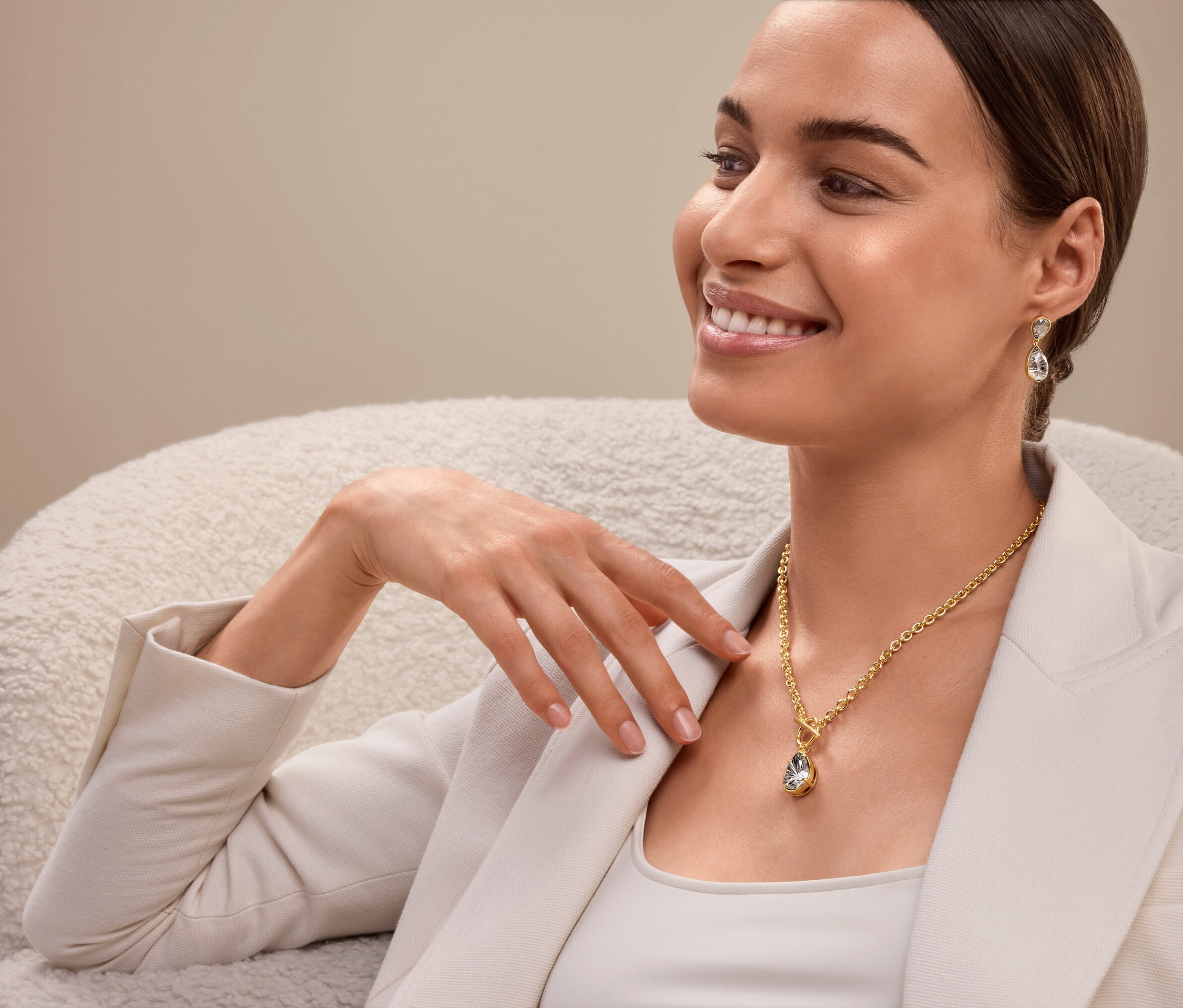 Žena sedí a má na sebe zlatý náhrdelník a náušnice.
