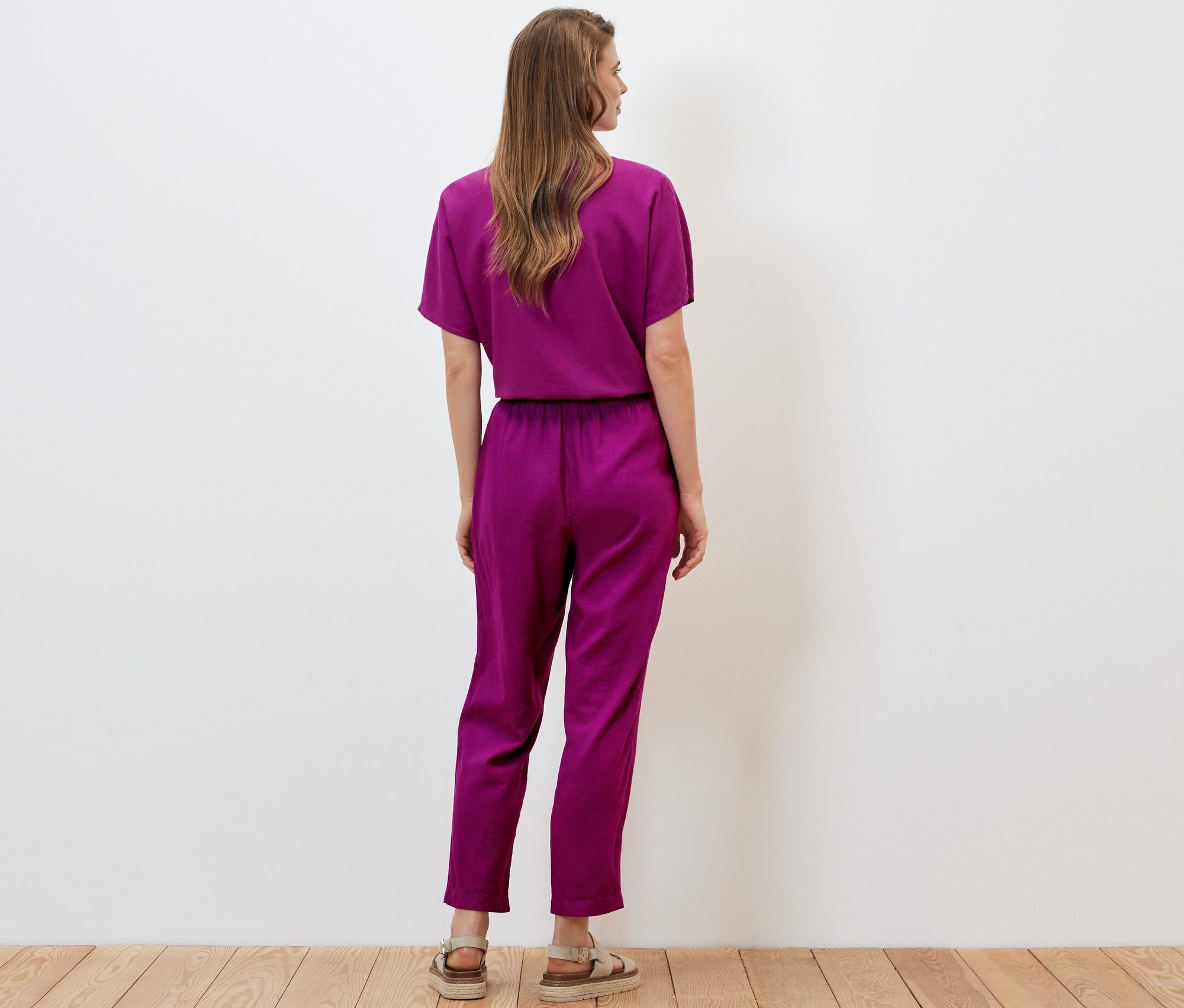 Žena stojí chrbtom a má na sebe ľanové nohavice bordovej farby.