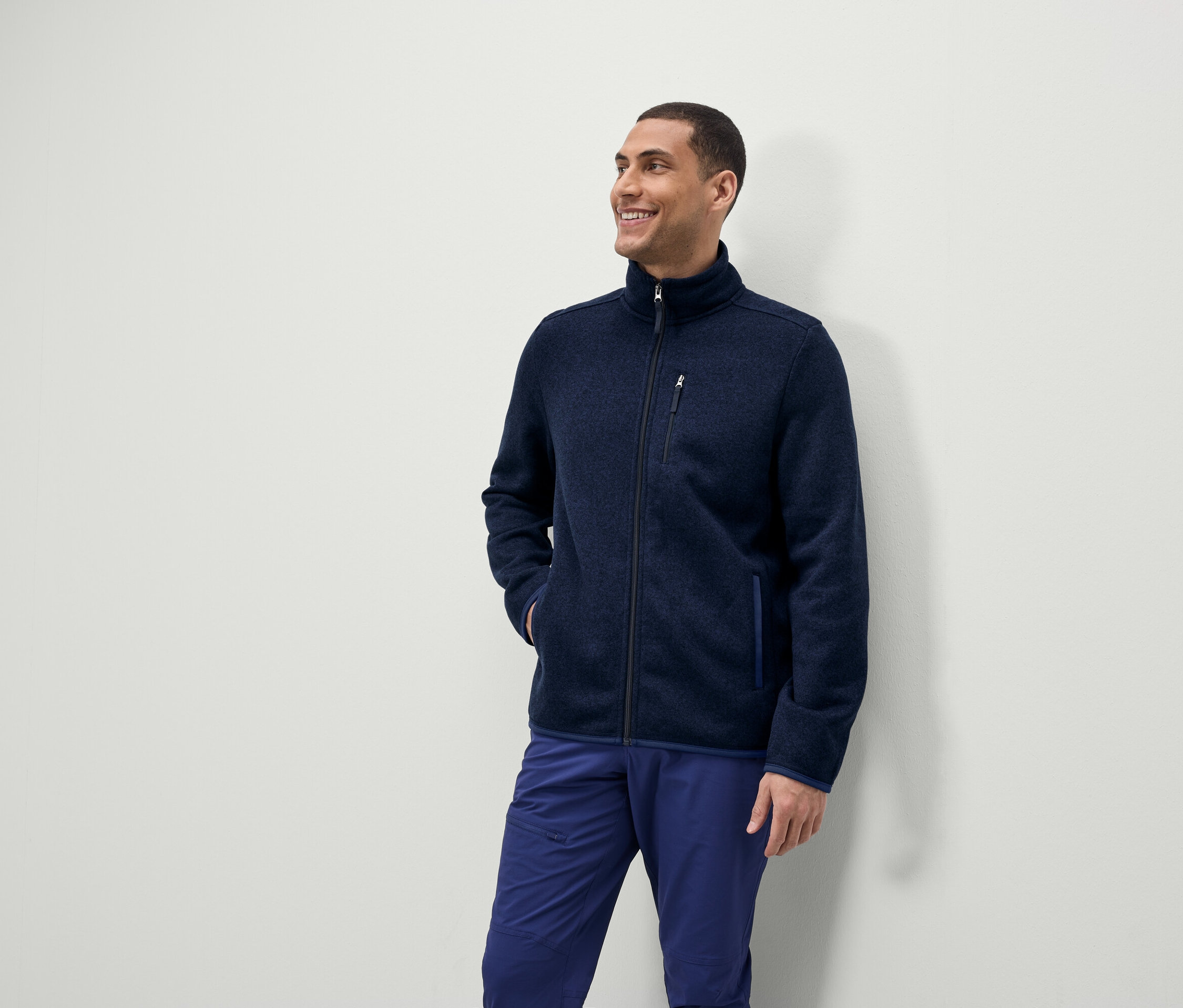 Muž sa usmieva a pozerá sa nabok, má na sebe modrú fleecovú bundu na zips a modré nohavice.