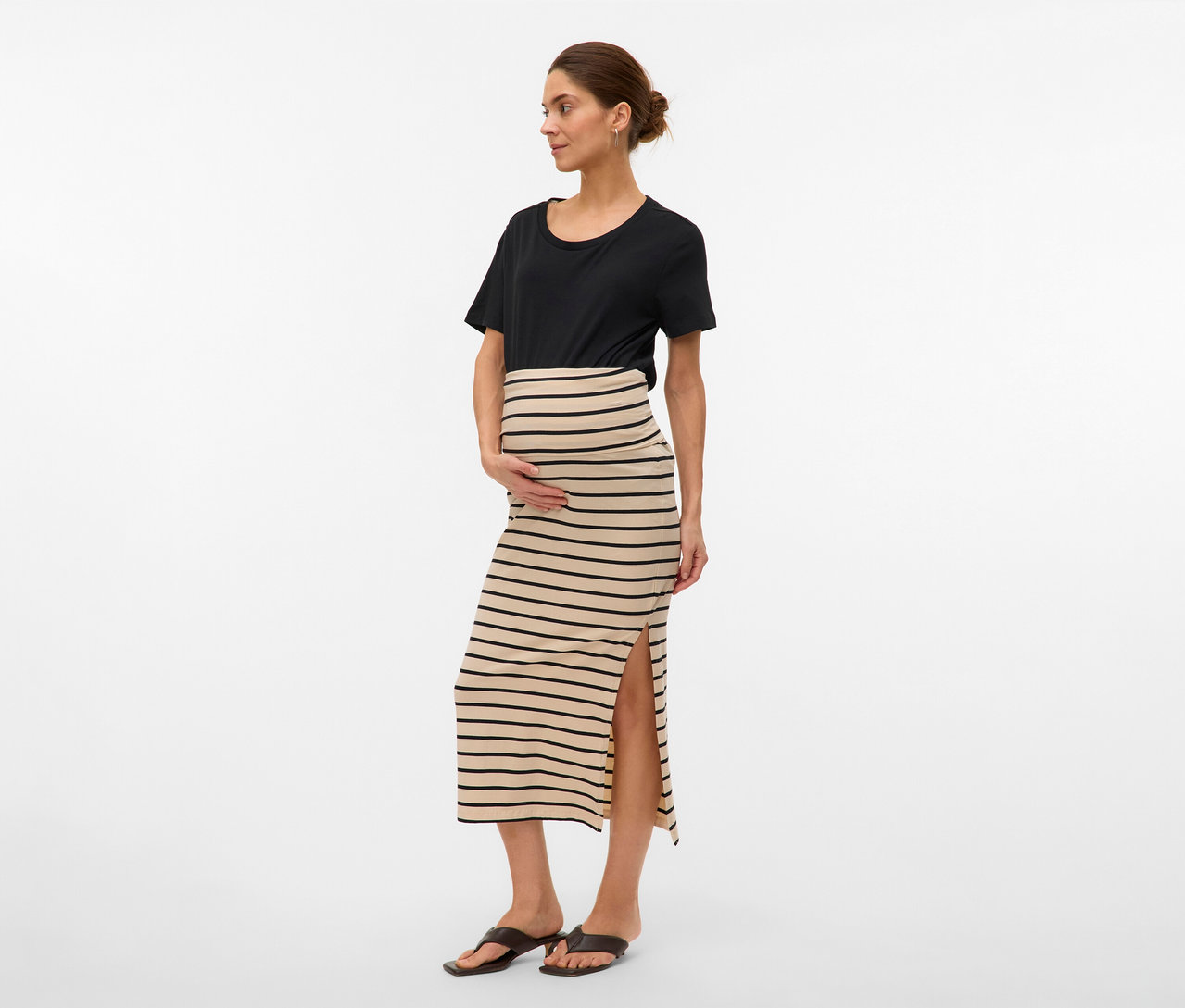 Žena v čiernom tričku a v pruhovanej maxi sukni MAMALICIOUS »MLEVA« s rozparkom. Drží ruky na bruchu.