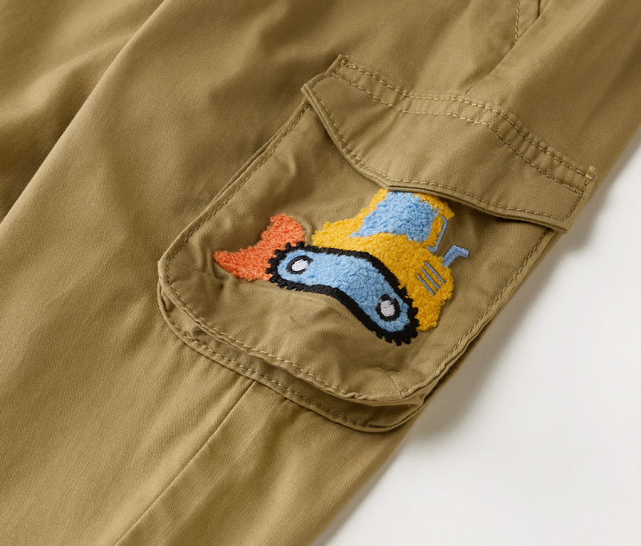 Detail záberu khaki cargo nohavíc s našitým vreckom zdobeným vyšívaným bagrom v oranžovej, žltej a modrej farbe.