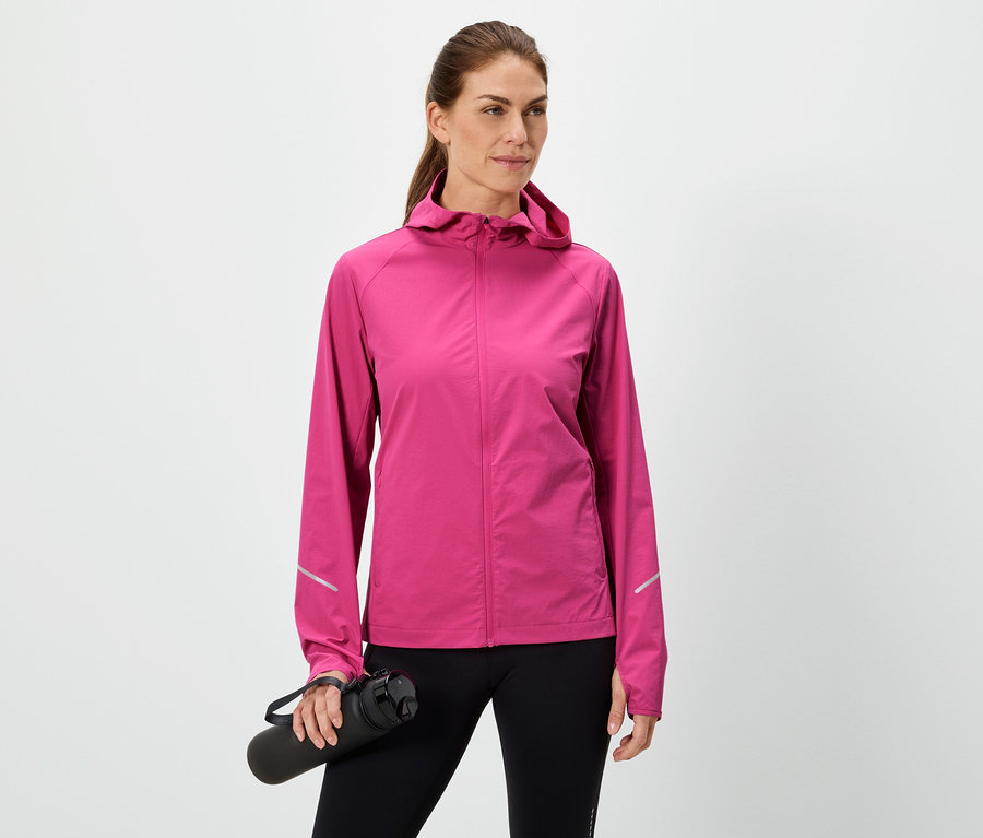 Žena drží čiernu fľašu na vodu, má na sebe ružovú bundu a čierne legíny na bielom pozadí.