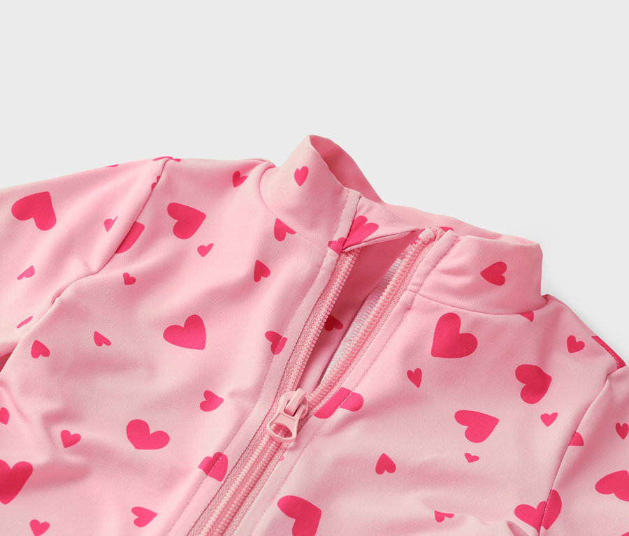 Detail ružového topu s červeným vzorom srdca a zipsom vpredu.