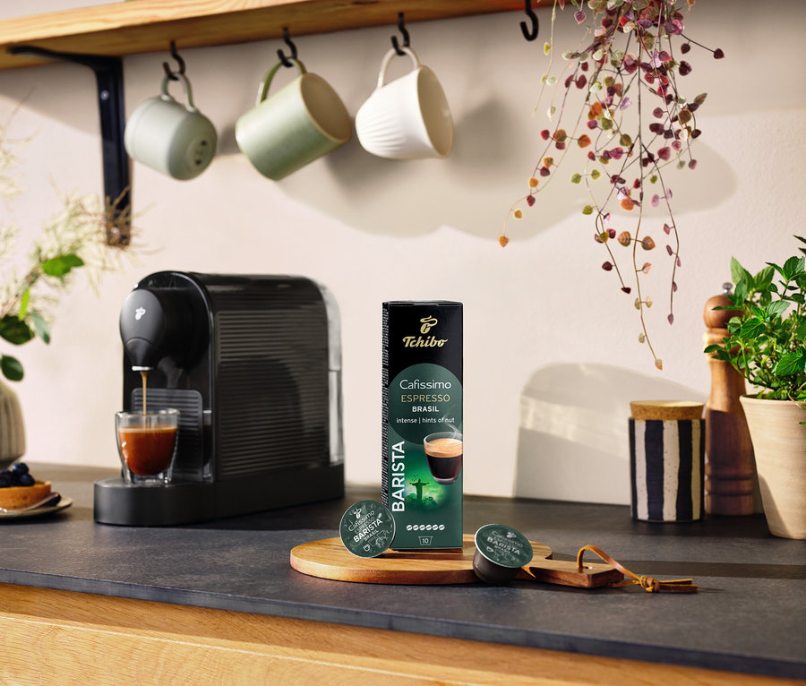 Čierny kávovar pripravuje kávu do pohára vedľa balenia kapsúl Espresso Brasil – 10 kapsúl.