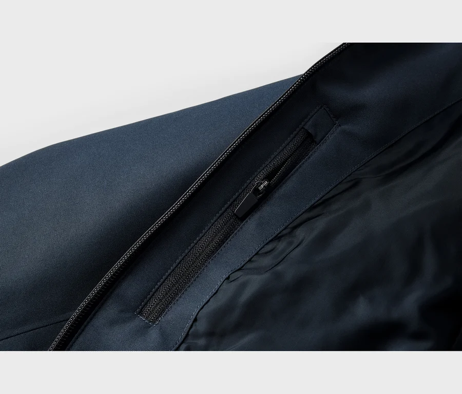 Detail tmavomodrej bundy zobrazujúci hlavný zips a čiastočne rozopnutý zips vrecka na vnútornej chlopni, odhaľujúci tmavomodrú podšívku.
