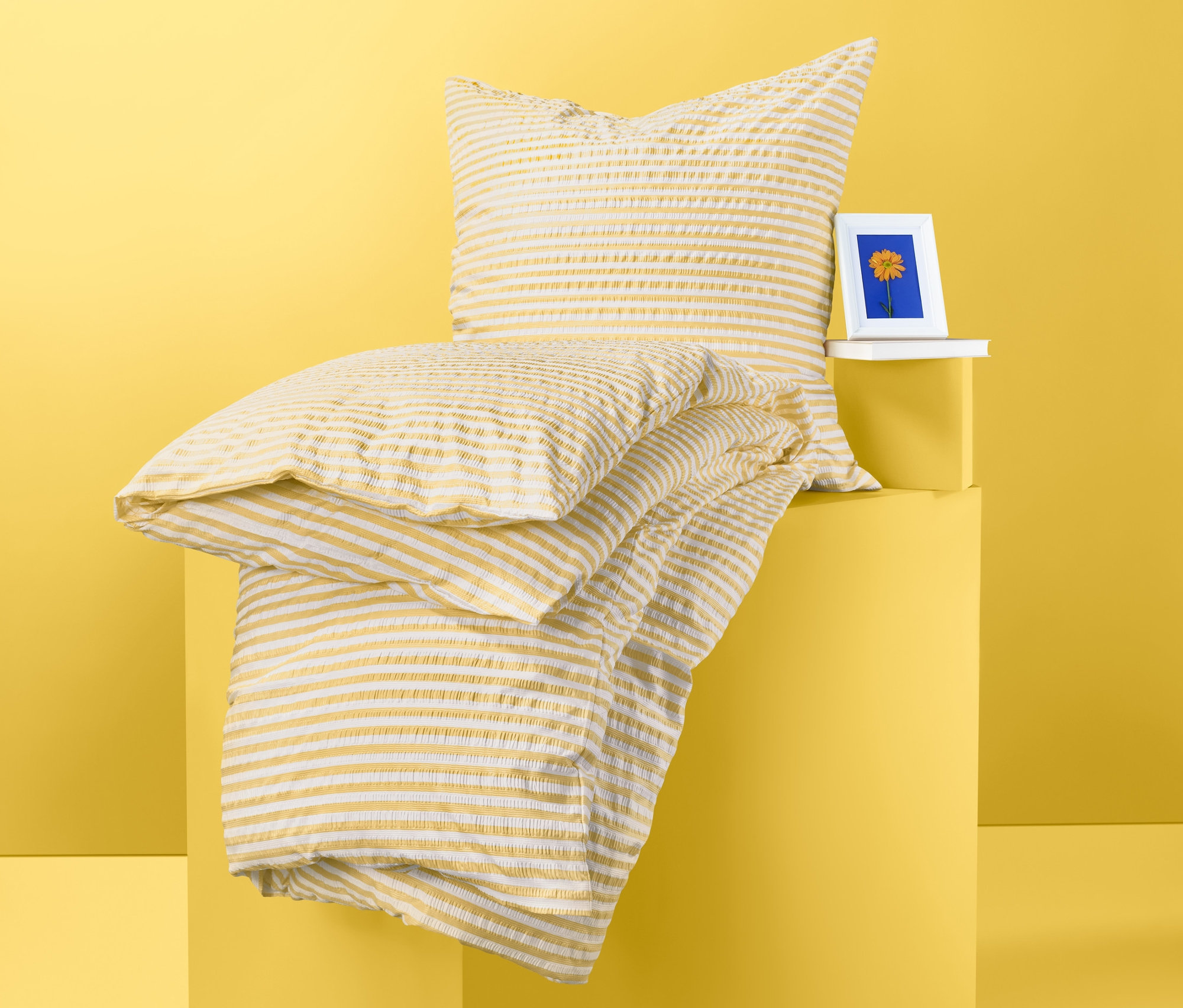 Na žltom pozadí ležia na sebe zložené krepové posteľné bielizne štandardnej veľkosti a krepové posteľné bielizne dvojlôžko.