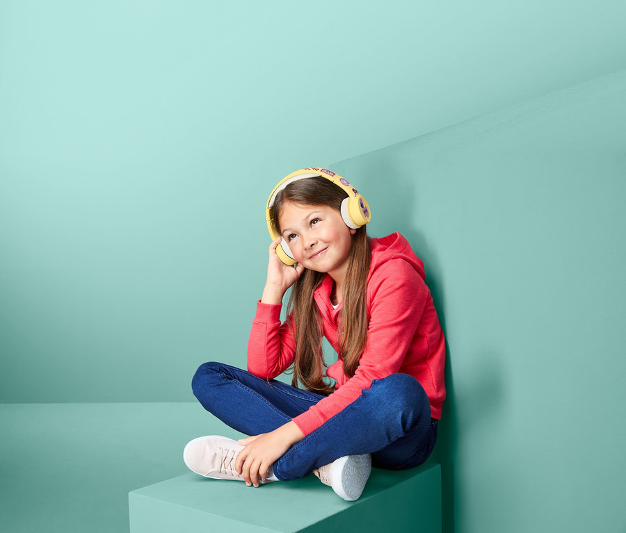 Dievča sedí a počúva hudbu cez bezdrôtové slúchadlá s Bluetooth® pre deti.