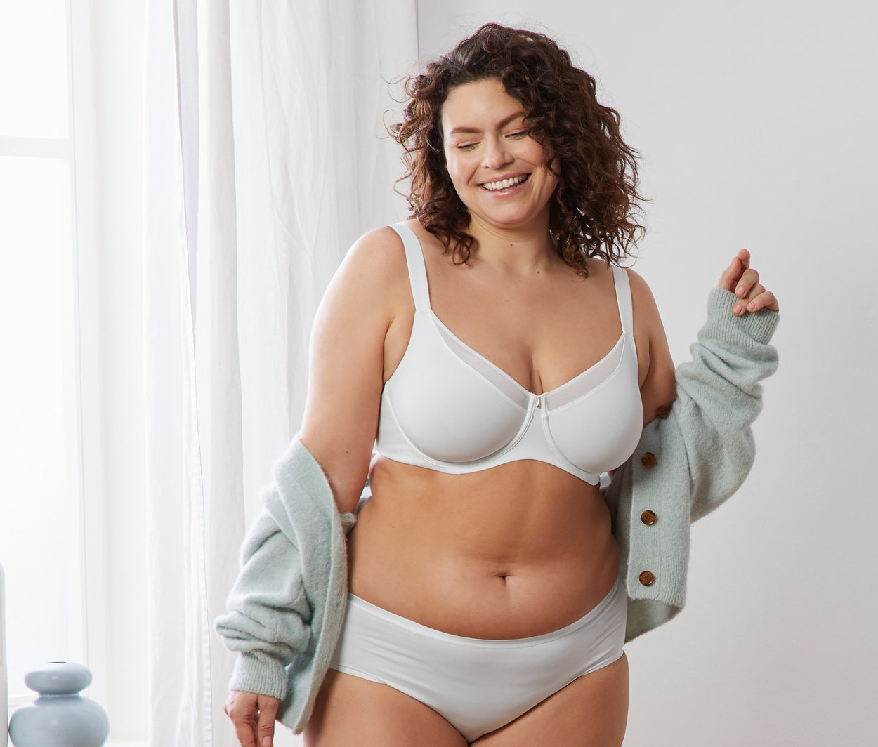 Žena sa usmieva a pózuje v bielej zmenšujúcej podprsenke.