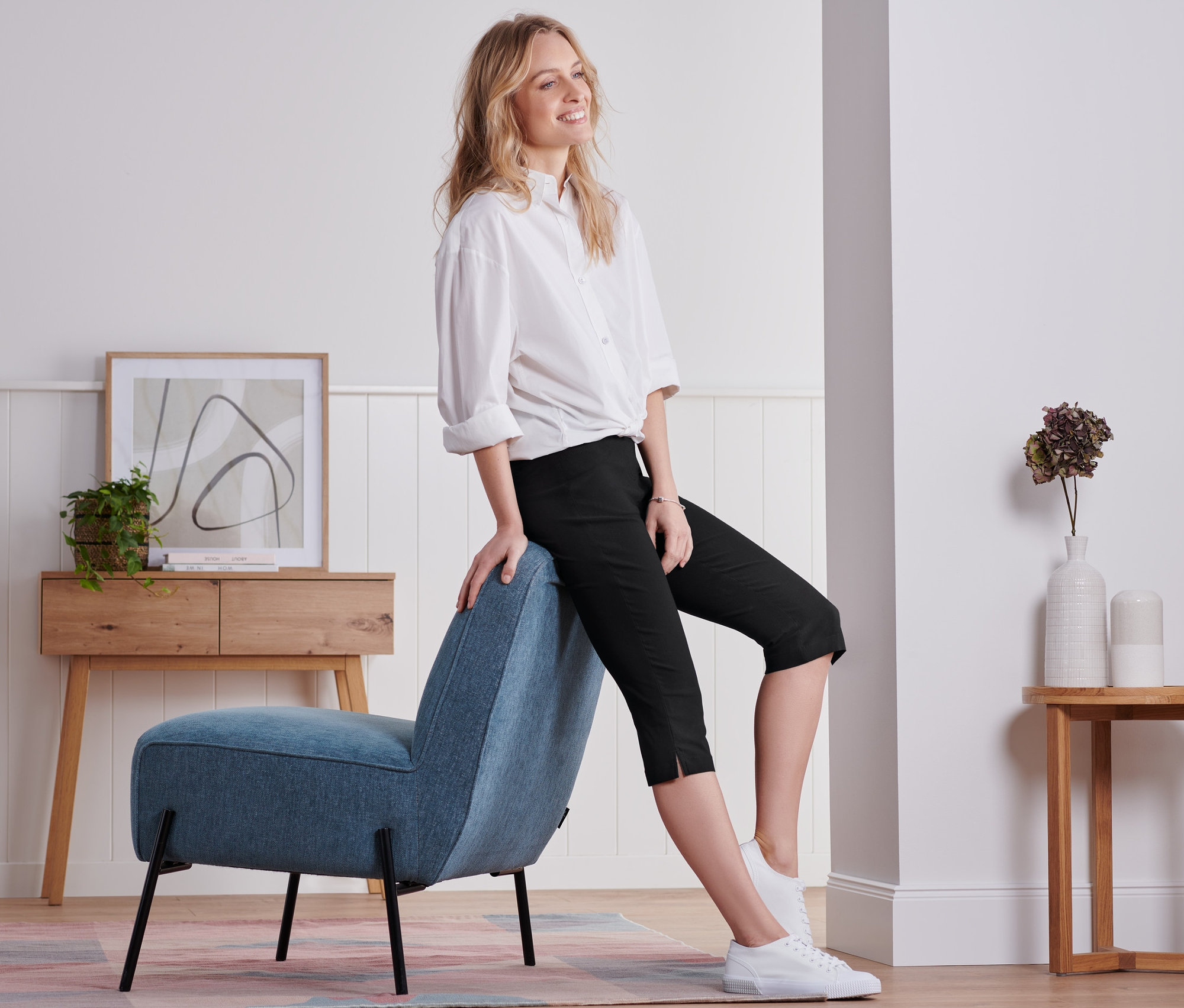 Žena sedí na modrom kresle a má na sebe čierne trojštvrťové nohavice.