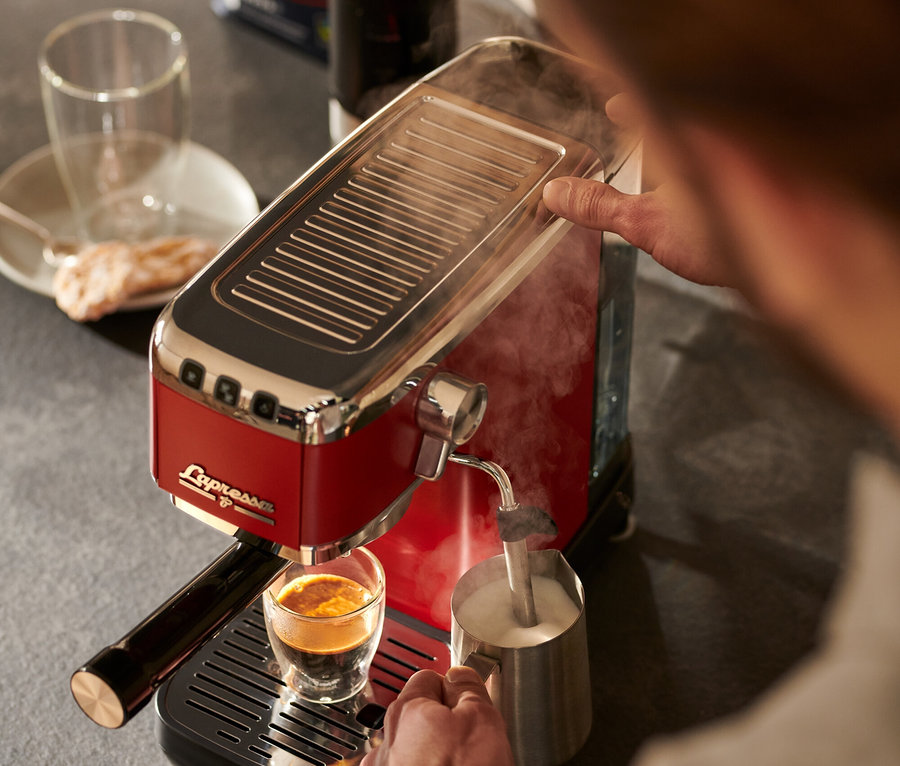 Muž používa červený pákový kávovar »Lapressa« na prípravu kávy a napenenie mlieka.