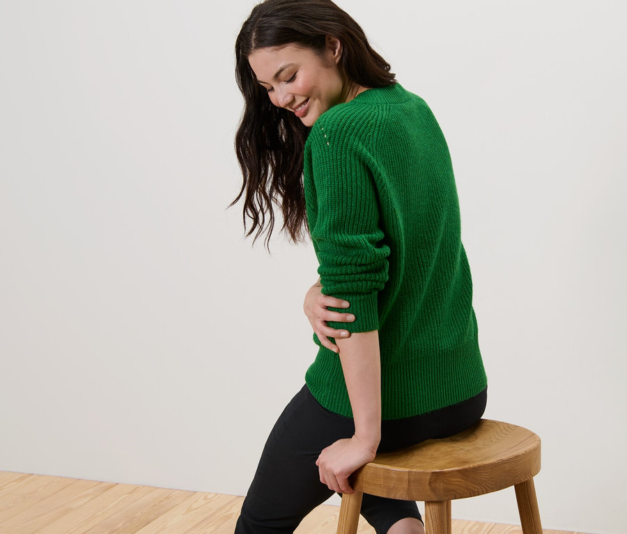 Žena sedí na stoličke a má na sebe zelený pletený pulóver.